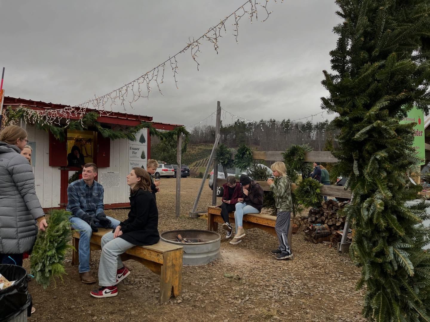 Families on benches around the bonfire beside the store, string lights overhead