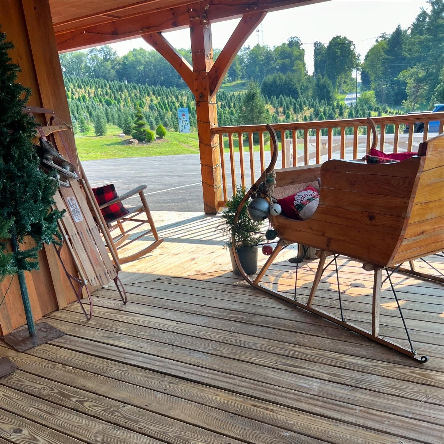 A wooden sleigh on the store porch, tree rows and the parking lot beyond the rail