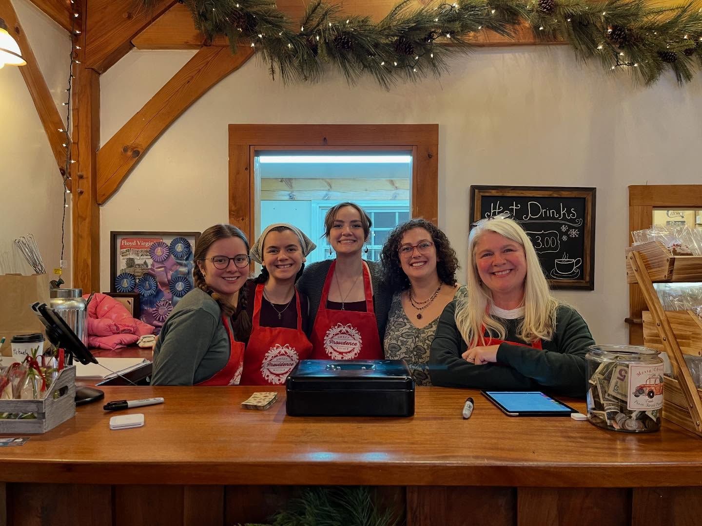 Five smiling staff behind the store counter under garland and string lights