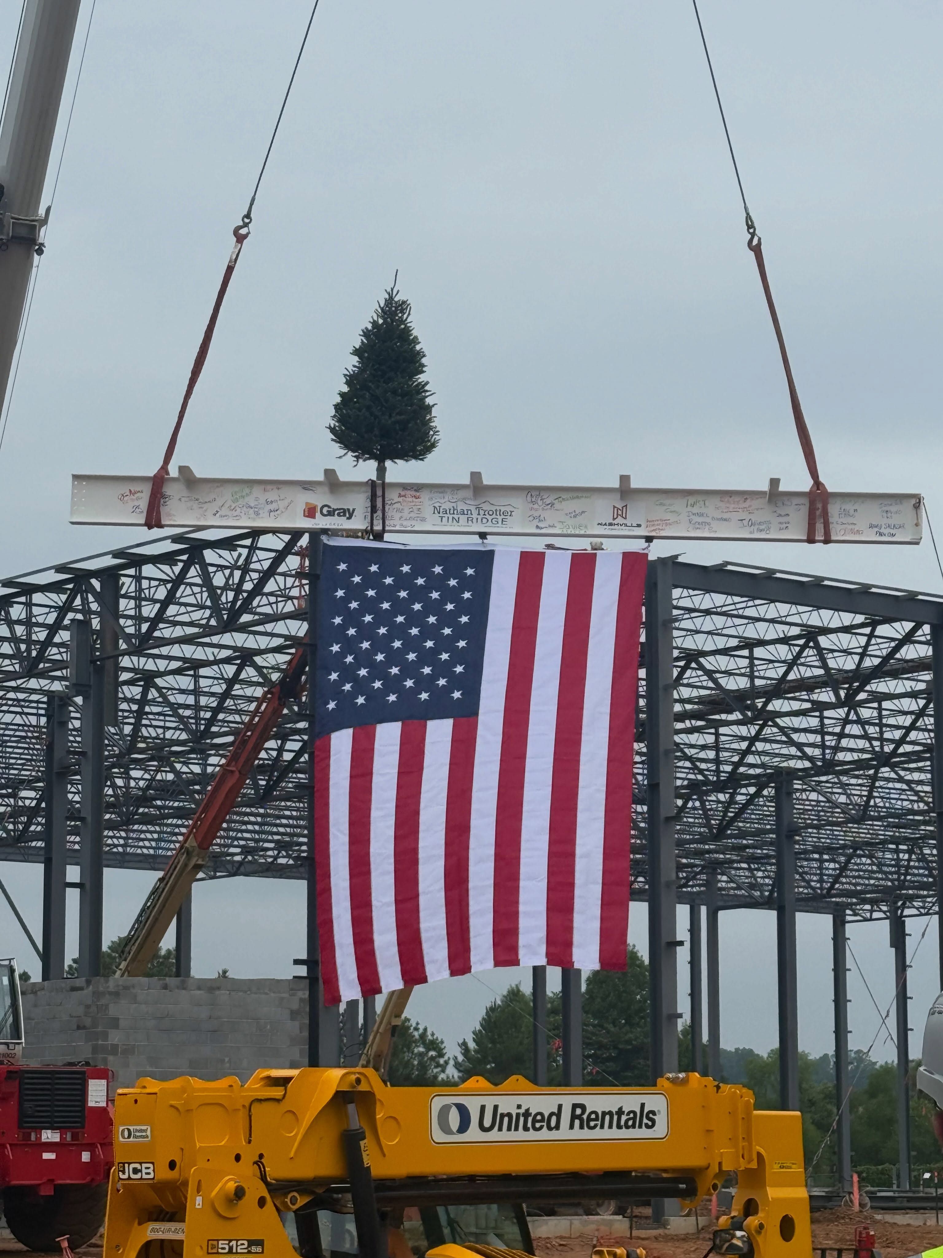 A Fraser Fir and an American flag hoisted on a steel beam at a building’s topping-out