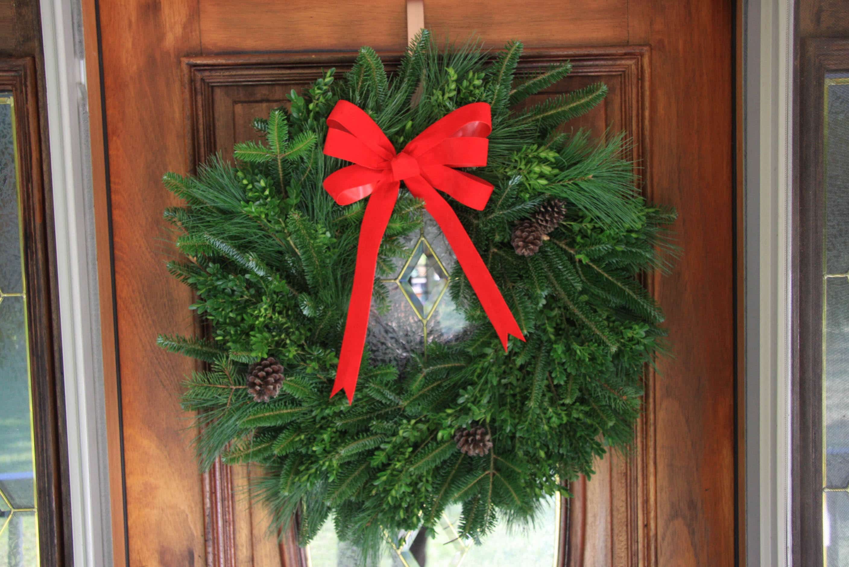 A fresh Fraser Fir wreath with a red velvet bow on a wooden door